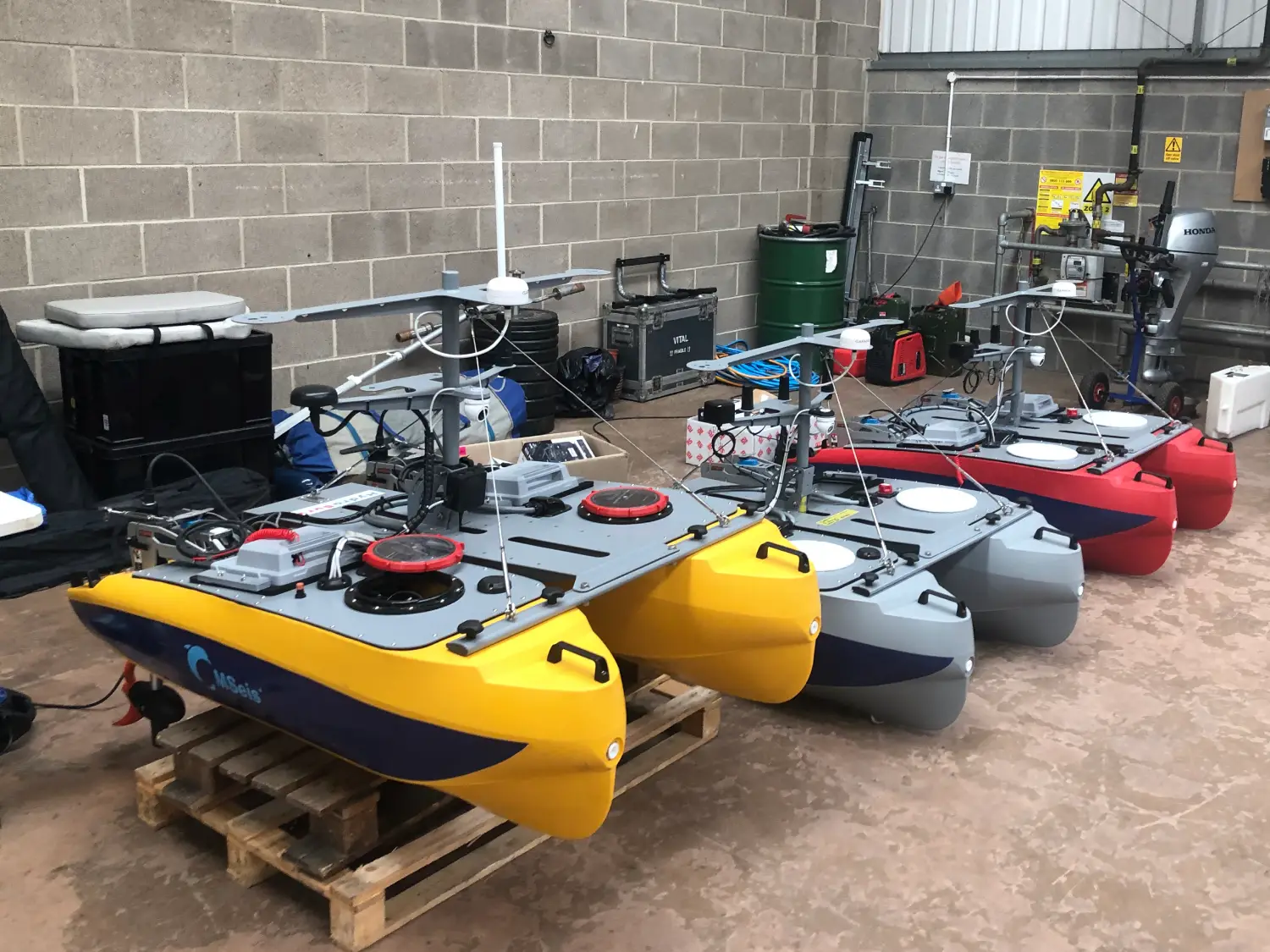 The three Mseis REAV-16 vessels inside a boat house. One is yellow, one is grey and one is red.